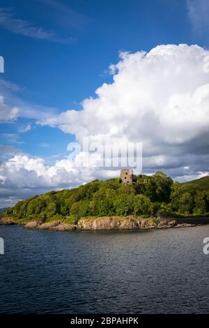 Château de Dunollie sur une colline verdoyante avec de grands nuages blancs en arrière-plan et une mer calme en premier plan, vue depuis le ferry entre l'île de Mull et Oban, en Écosse Banque D'Images