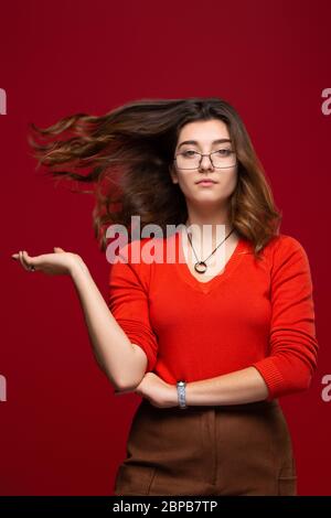 Jeune fille étudiante ou femme d'affaires en lunettes avec cheveux volants isolés sur fond rouge. Le concept de confiance en soi et d'estime de soi Banque D'Images
