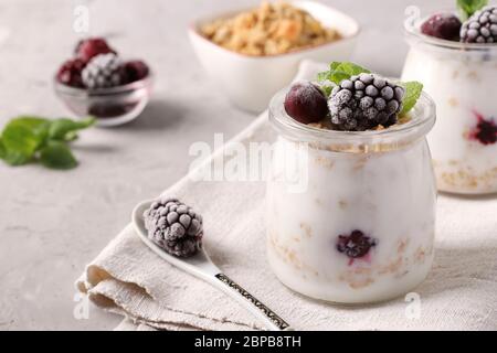 Muesli au miel croustillant de granola avec yaourt naturel, baies congelées et menthe dans des pots en verre sur fond gris, nourriture saine Banque D'Images