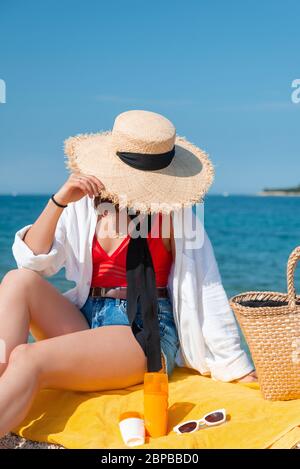 femme assise sur une couverture jaune à la plage de la mer en tenue d'été Banque D'Images