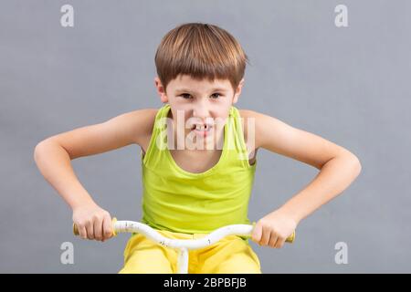 Enfant sur un vélo sur fond gris. Un petit garçon drôle joue un motard. Banque D'Images