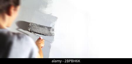 Craftswoman avec de grandes peintures à rouleaux mur blanc avec peinture gris-argent entreprise de peinture formation profession d'enseignement faites-le vous-même outils Banque D'Images