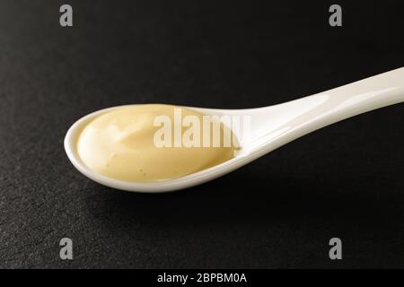 Mayonnaise classique dans une cuillère en porcelaine chinoise blanche sur une planche à servir en pierre noire. Sauces et assaisonnements pour la viande, le poisson et les légumes. Vue avant. Banque D'Images