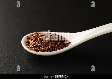 Graines de lin dans une cuillère en porcelaine chinoise blanche sur une plaque de service en pierre noire. Sauces et assaisonnements pour la viande, le poisson et les légumes. Vue avant. Banque D'Images