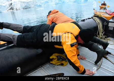 Un touriste portant un costume sec et un gilet de sauvetage débarquant ou embarquant d'un kayak à un bateau à côtes (zodiaque) à Svalbard dans l'Arctique norvégien. Banque D'Images