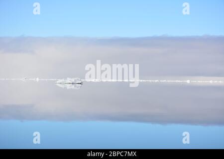 Vue imprenable sur la glace de mer flottante lors d'une journée d'été calme à Svalbard, avec le ciel pastel reflété dans la surface de l'eau. Banque D'Images