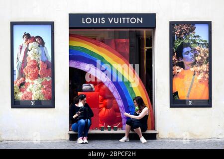 Deux jeunes amies féminines assises devant la fenêtre du magasin phare Louis Vuitton, font une pause détente et prennent leur masque médical pendant le confinement du coronavirus Covid 19. Rome, Italie, Europe, Union européenne, UE. Banque D'Images