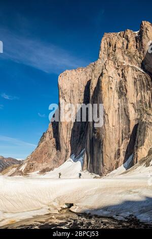 Vue lointaine de deux alpinistes qui s'éxpensèment sous une grande falaise de montagne. Banque D'Images