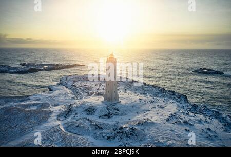 Vue sur la tour de phare en pierre de drone sur fond de paysage marin magnifique et de terrain enneigé pendant le coucher du soleil Banque D'Images