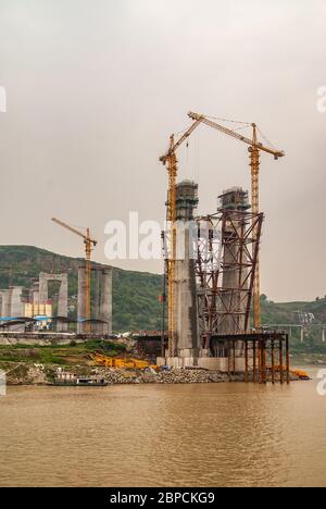 Fengdu, Chongqing, Chine - 8 mai 2010 : fleuve Yangtze. Tour de suspension en béton pour pont en construction avec de hautes grues jaunes sur une manne brune Banque D'Images