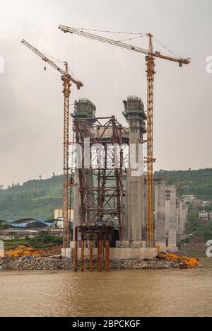 Fengdu, Chongqing, Chine - 8 mai 2010 : fleuve Yangtze. Tour de suspension en béton pour pont en construction avec de hautes grues jaunes sur une manne brune Banque D'Images