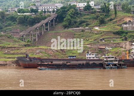 Fengdu, Chongqing, Chine - 8 mai 2010 : fleuve Yangtze. Bateau à charbon avec d'autres grands bateaux sur le rivage brun-vert avec agriculture, long escalier, an Banque D'Images