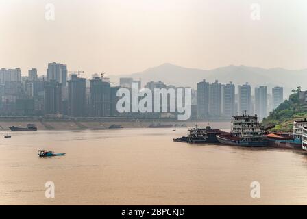 Fengdu, Chongqing, Chine - 8 mai 2010 : fleuve Yangtze. Paysage urbain de bâtiments élevés sur le rivage derrière une large eau brune avec certains navires naviguant et Banque D'Images