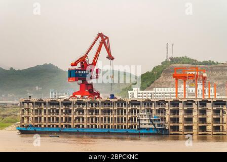 Huangqikou, Chongqing, Chine - 8 mai 2010 : fleuve Yangtze. La grue rouge et bleue décharge la barge bleue au quai à plusieurs niveaux du port. Colline verte sous smog sk Banque D'Images