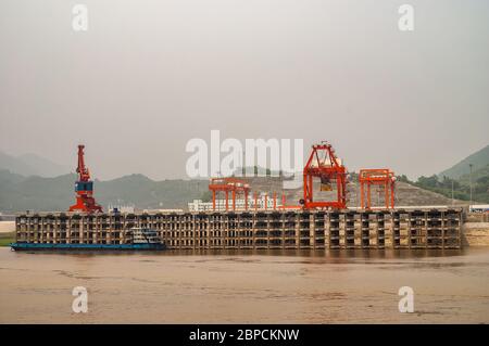 Huangqikou, Chongqing, Chine - 8 mai 2010 : fleuve Yangtze. Paysage de grues sur quai à plusieurs niveaux derrière l'eau brune. Barge ancrée, vert f Banque D'Images