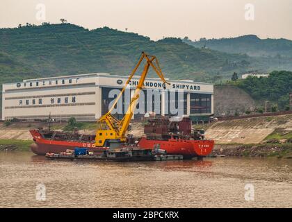 Myaoyinan, Chongqing, Chine - 8 mai 2010 : fleuve Yangtze. Construction avec grue jaune sur ponton de bateau dans l'eau brune au chantier naval de Chiandong. Gree Banque D'Images