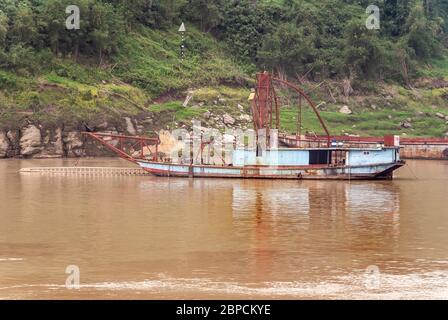 Huangqikou, Chongqing, Chine - 8 mai 2010 : fleuve Yangtze. Navires de dragage inactifs bleu clair amarrés le long de rives boisées vertes sur des eaux brunes. Banque D'Images