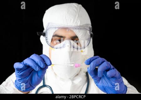 Technologue en soins médicaux tenant le kit de prélèvement d'écouvillons COVID-19, portant des gants de protection PPE blancs, tube à essai pour prélever des échantillons de patient . Banque D'Images