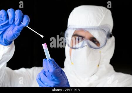 Technologue en soins médicaux tenant le kit de prélèvement d'écouvillons COVID-19, portant des gants de protection PPE blancs, tube à essai pour prélever des échantillons de patient . Banque D'Images