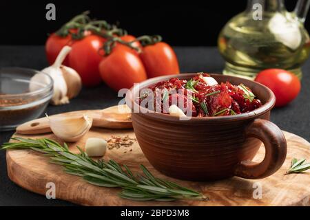Tomates séchées au soleil avec ail, romarin et épices dans un bol en argile sur un tableau de découpe en bois d'olive. Banque D'Images