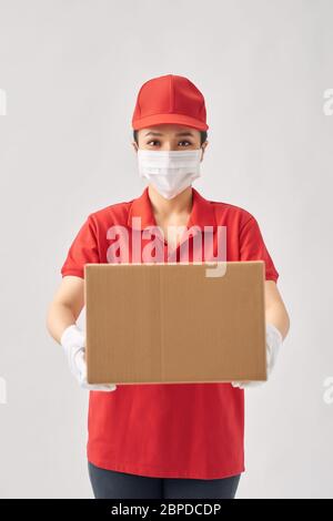 Un messager en uniforme portant des gants médicaux en caoutchouc et un masque médical tient une boîte en papier d'aliments sur un fond blanc. Banque D'Images