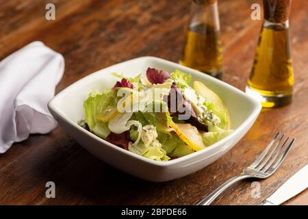 Salade fraîche de printemps avec laitue et tranches de poires et fromage bleu dans un bol blanc sur table et serviette en bois, huile d'olive. Banque D'Images