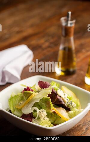 Salade fraîche de printemps avec laitue et tranches de poires et fromage bleu dans un bol blanc sur table et serviette en bois, huile d'olive. Banque D'Images