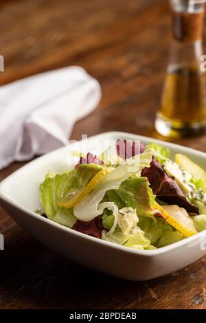 Salade fraîche de printemps avec laitue et tranches de poires et fromage bleu dans un bol blanc sur table et serviette en bois, huile d'olive. Banque D'Images