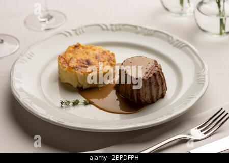 Filet mignon de filet avec gratin de pommes de terre et sauce au poivre vert sur blanc avec verre à vin sur fond flou. Banque D'Images