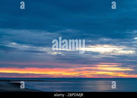 Le ciel de l'aube au-dessus du parc éolien offshore de Thanet au large de la côte du Kent en Angleterre, vu de Ramsgate. La mer, avec les éoliennes à l'horizon contre une couche vive de nuages orange et rouge, avec un ciel sombre et nuageux au-dessus. Banque D'Images