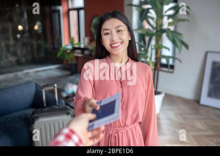 Une femme gaie aux cheveux sombres prend des billets d'avion des mains de sexe masculin, souriant Banque D'Images