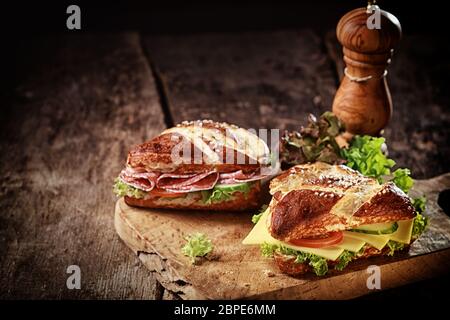 Croque-monsieur avec pain de lye brun croustillant et fromage, salami, laitue, tomate et concombre, sur une vieille planche à grattes avec un moulin à poivre en bois et un Banque D'Images