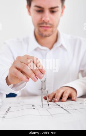 Closeup Portrait of a young male architect working on blueprints étalé sur une table Banque D'Images
