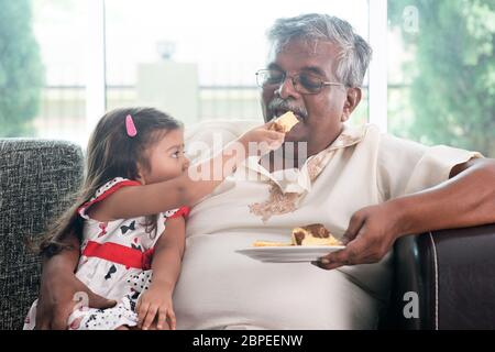 Portrait de la famille indienne à la maison. Petit-enfant nourrissant un gâteau au beurre pour les grands-parents. Grand-père et petite-fille. Les Asiatiques qui vivent le mode de vie. Banque D'Images