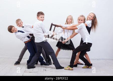 Enfants jouant la tug de chaise - filles contre garçons sur fond blanc. Concept de l'école garçons et filles confrontation Banque D'Images