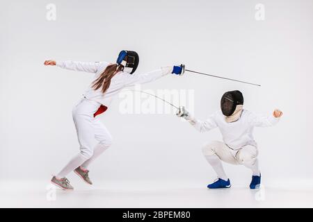 La femme et l'homme portant tenue d'escrime pratiquant avec épée contre l'arrière-plan gris studio Banque D'Images