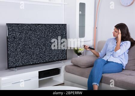 Vue arrière d'une femme sur canapé obtenir frustré avec Glitch écran de télévision à la maison Banque D'Images
