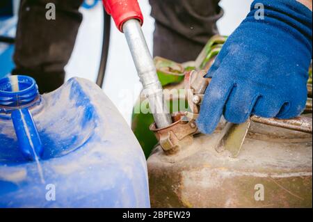 Homme adulte remplit une voiture avec l'essence à une station essence en hiver. l'homme de la buse de ravitaillement en tenant à la main, verser le liquide dans le canister et fu Banque D'Images