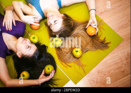 Deux jeunes femmes au physique athlétique sport s'allonger sur le sol sur un tapis de yoga. Fitness petite fille avec des fruits, du style de vie pour perdre du poids et des régimes alimentaires, une bonne nutriti Banque D'Images