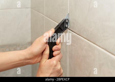 Les mains des hommes à l'aide d'un couteau retirer le vieux coulis. Remplacer le coulis entre les carreaux. Le ratissage des carreaux pour regrouting. Banque D'Images