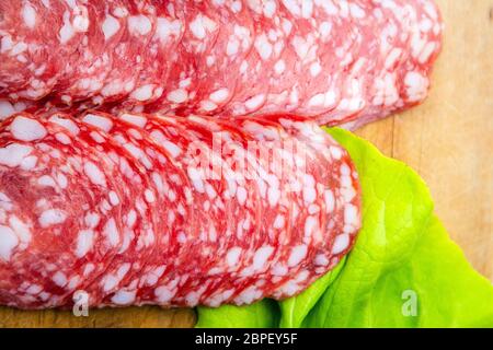Gros plan de tranches rondes de salami avec de la graisse blanche à côté de la salade verte sur une planche à découper en bois. Fines tranches de délicieux salami Banque D'Images