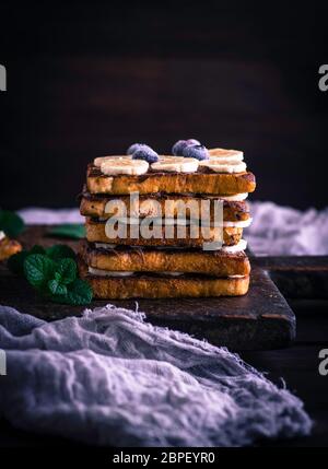 Poêlée de morceaux de pain blanc dans un œuf avec le lait et enduit de chocolat, pain doré avec une banane sur une planche en bois brun Banque D'Images