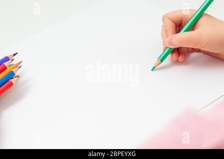 Main d'enfant avec un crayon vert sur fond blanc. Main de l'enfant qui dessine sur une feuille avec un crayon vert. Maquette. Copier l'espace. Banque D'Images