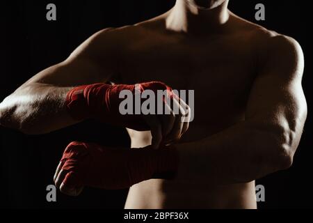 Gros plan sur les mains d'un jeune boxeur qui serpente les bandages rouges avant un match, un combat ou une formation. Banque D'Images