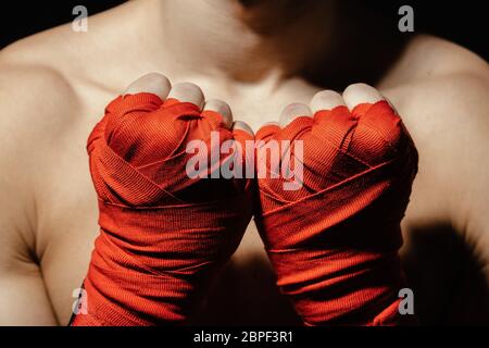 Gros plan des mains boxeurs dans des bandages rouges près de la poitrine, prêts pour un combat. Concept. Bras forts et poings serrés Banque D'Images