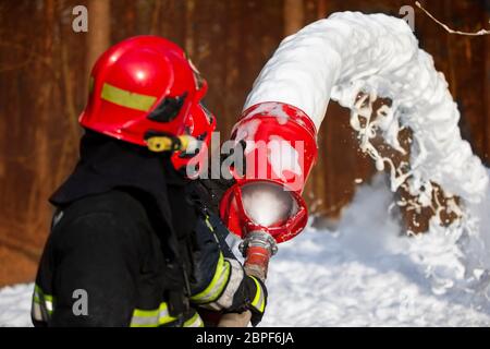 Les pompiers éteignent un incendie. Secouristes avec tuyaux d'incendie avec mousse. Banque D'Images