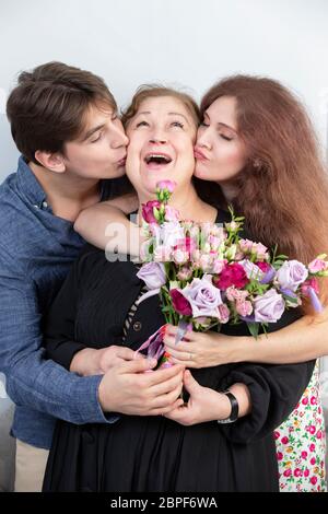 Vacances à la femme. Femme âgée avec un bouquet de fleurs entouré d'enfants. Petit ami et petite amie embrassent la grand-mère. Les enfants félicitent Banque D'Images