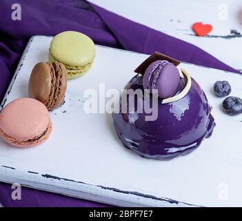 Gâteau rond lilas avec des macarons sur une planche de bois blanc, vue du dessus Banque D'Images