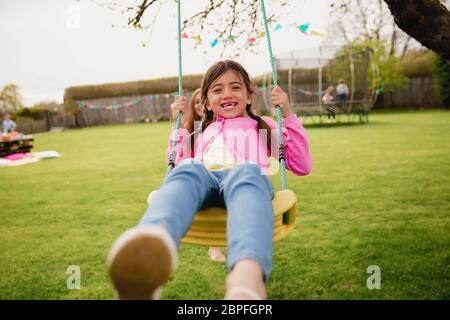 Petite fille jouant à l'extérieur sur une balançoire alors que son aide à sa mère et la pousse. Elle a l'amusement et de plaisir. Banque D'Images