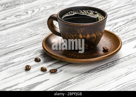 Café noir fort dans une tasse en céramique sur une table en bois clair. Il y a e peu de grains de café sur la table. Banque D'Images